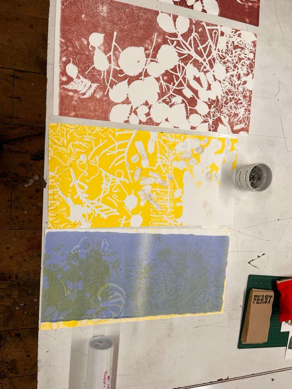 Yellow, blue, and red-brown lithography test prints on a studio table